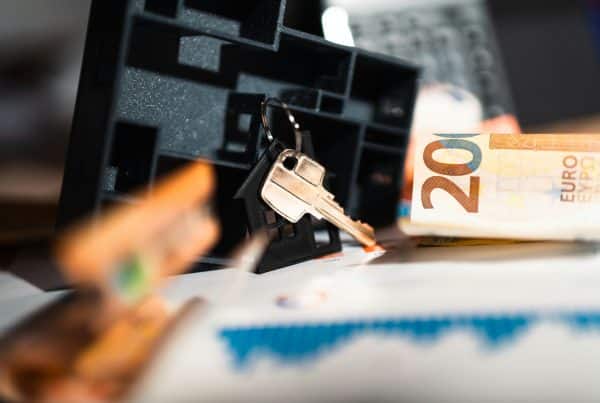 Close-up of house keys on a keychain with a house-shaped keyring, euro banknotes, and financial documents in the background.