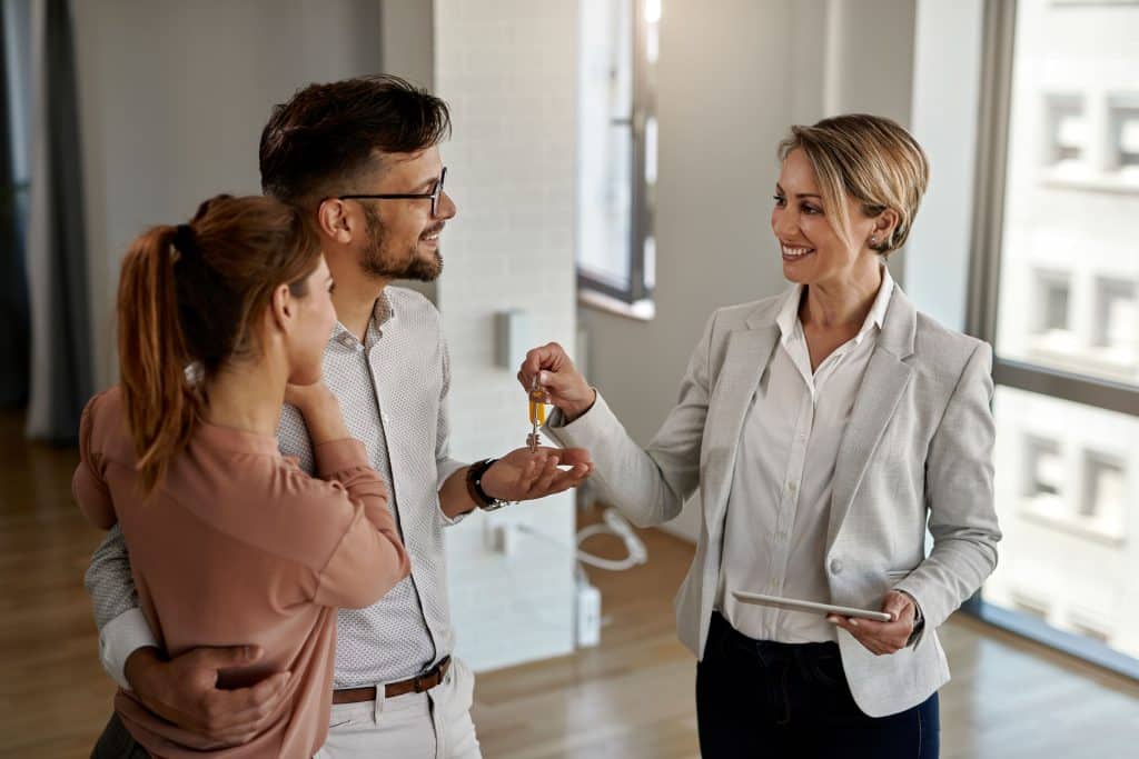 happy real estate agent giving keys couple who is buying their new home