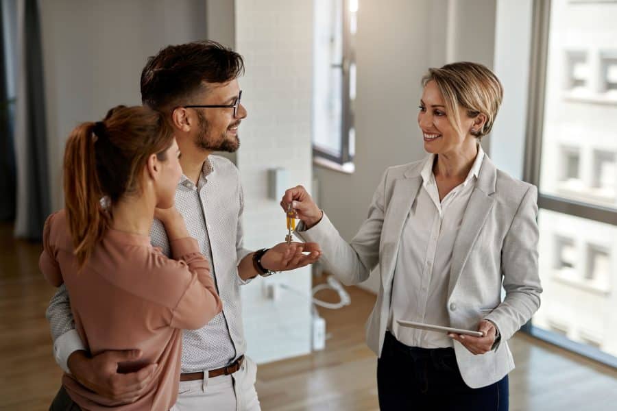 happy real estate agent giving keys couple who is buying their new home