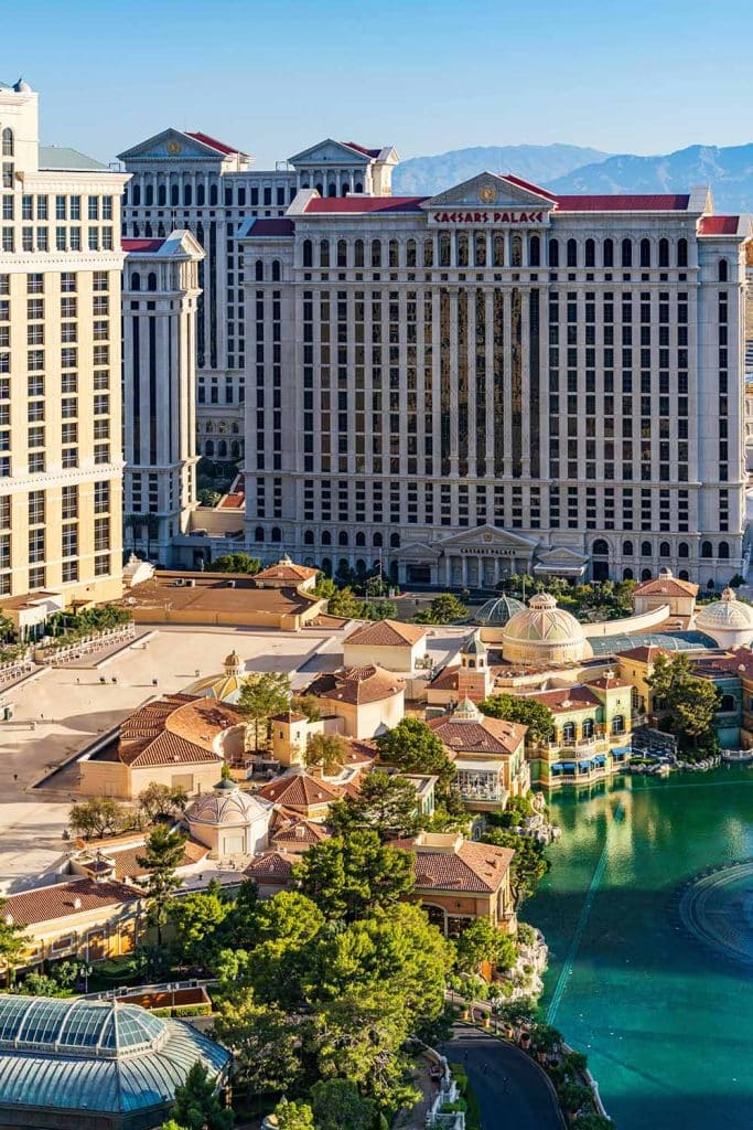 An aerial view of the "CAESARS PALACE" hotel, smaller buildings, and a bright green lake.