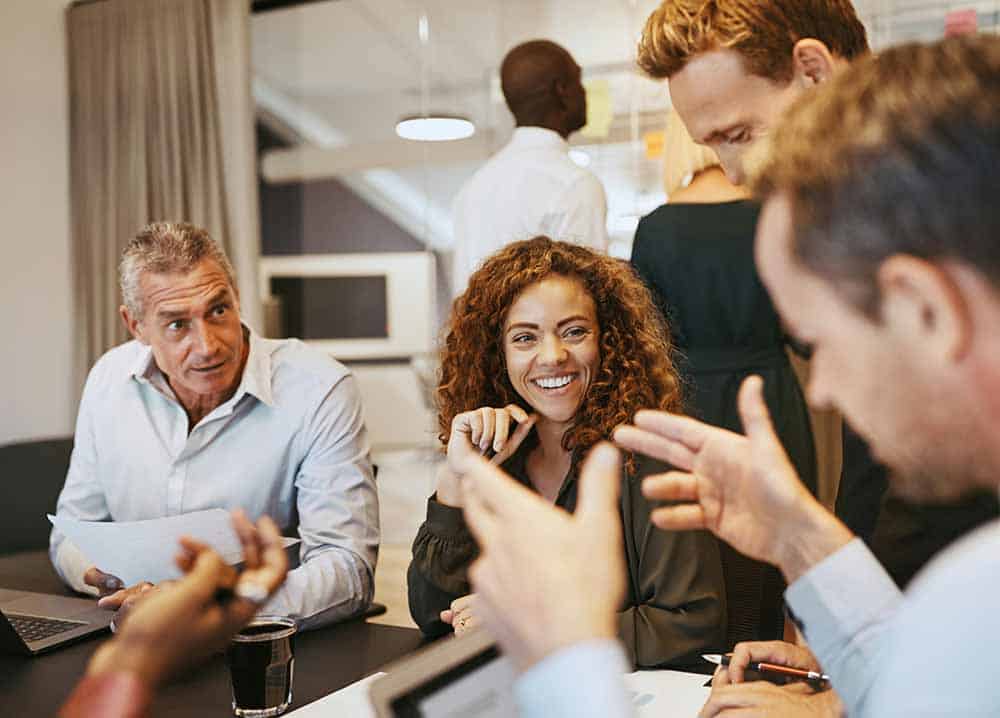 A diverse group of five professionals in an office, with a woman with curly hair smiling and laughing.
