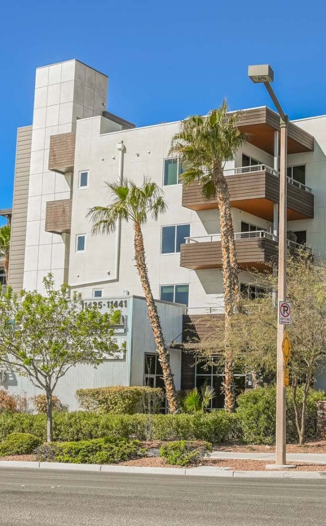 A modern white building with brown balconies, two palm trees, and a street sign that says "NO PARKING ANYTIME."