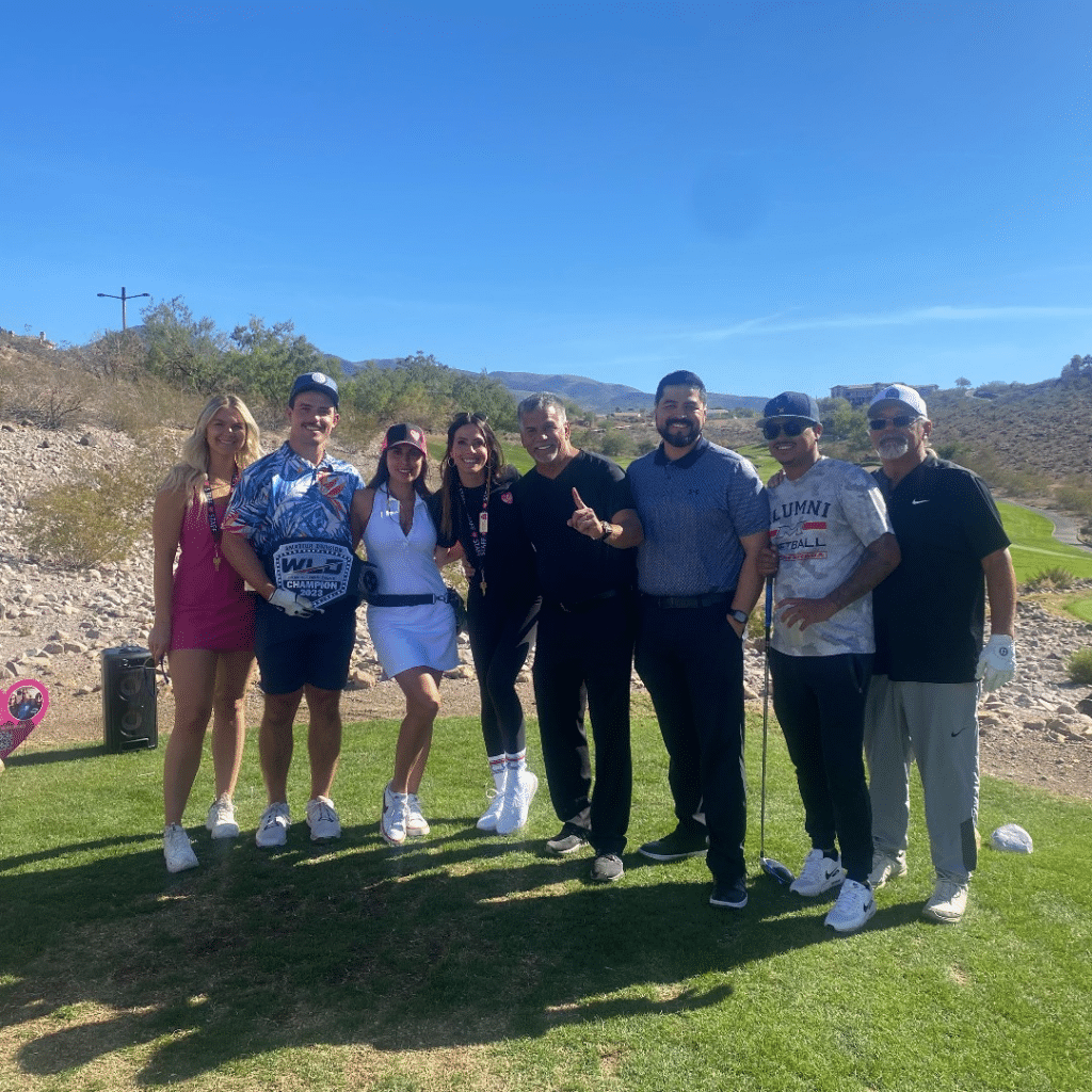 Eight people on a golf course, one holding a "WLD Champion 2023" belt, smiling at the camera.