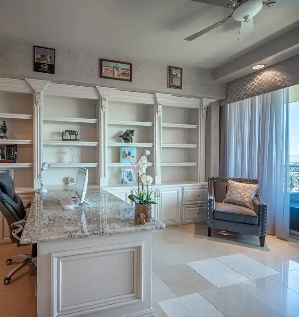 A home office with a white granite desk, a computer, a rolling chair, and a large built-in bookshelf.