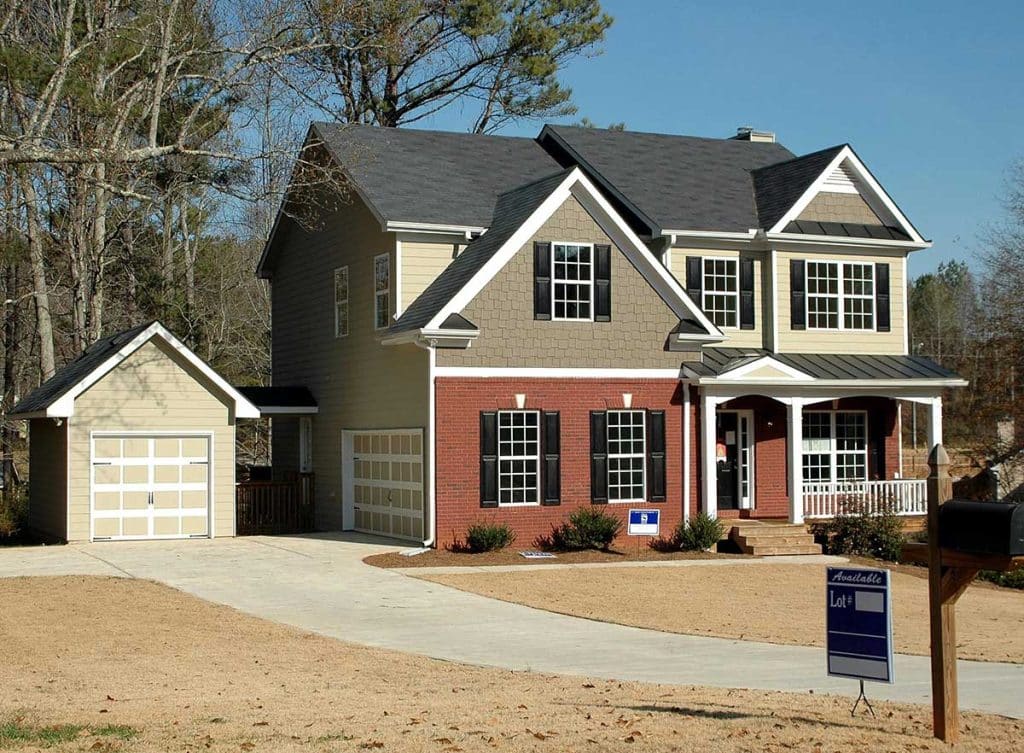 A large, two-story house with red brick and tan siding, two garages, and an "Available Lot" sign.