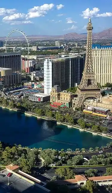 An aerial view of the Las Vegas Strip, with the Eiffel Tower replica, a lake, and a Ferris wheel.